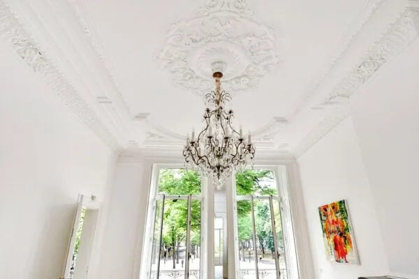 Luxe interieur aan het Lange Voorhout met sierplafond, kristallen kroonluchter en uitzicht op een groene laan.